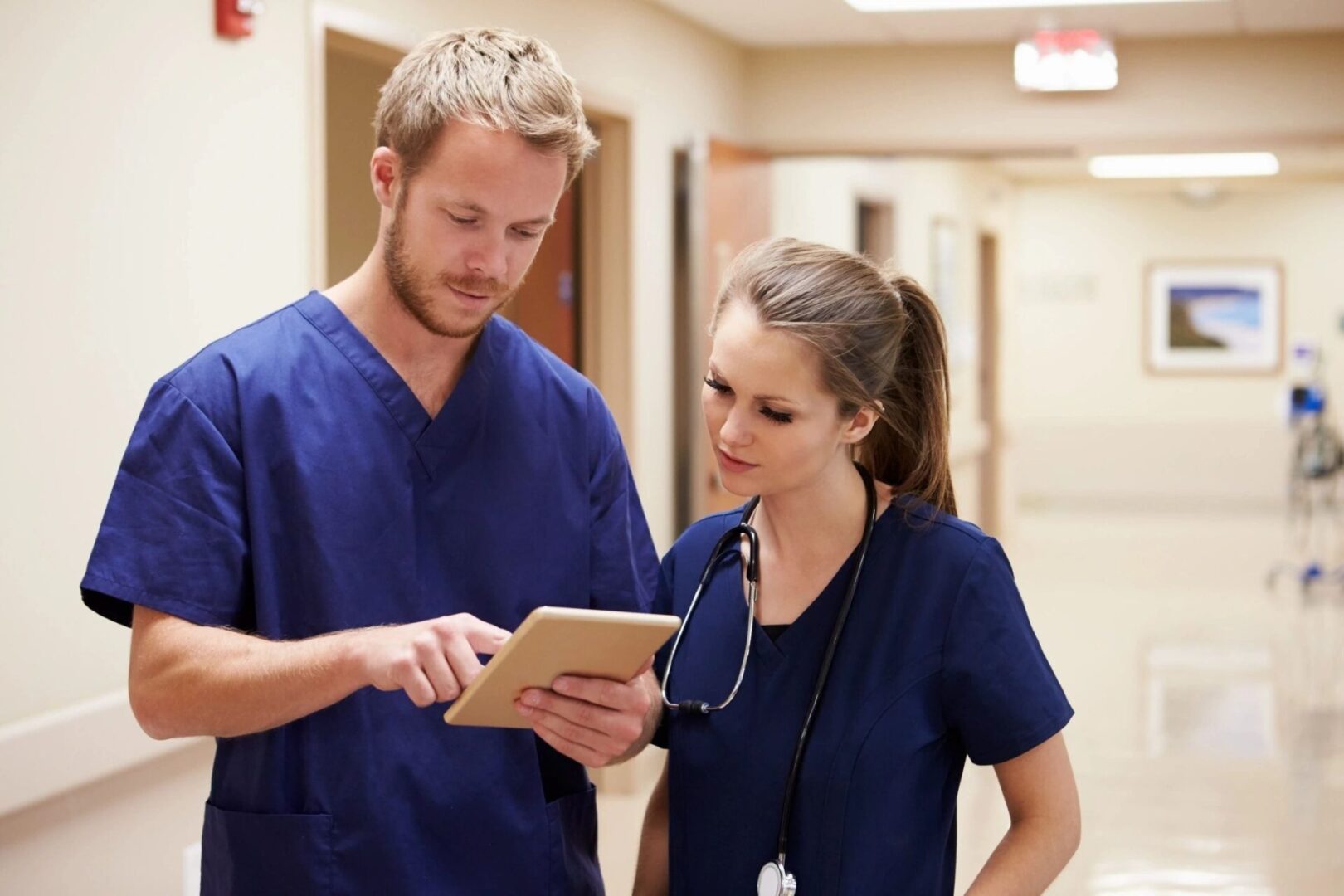 A man and woman in scrubs looking at an ipad.